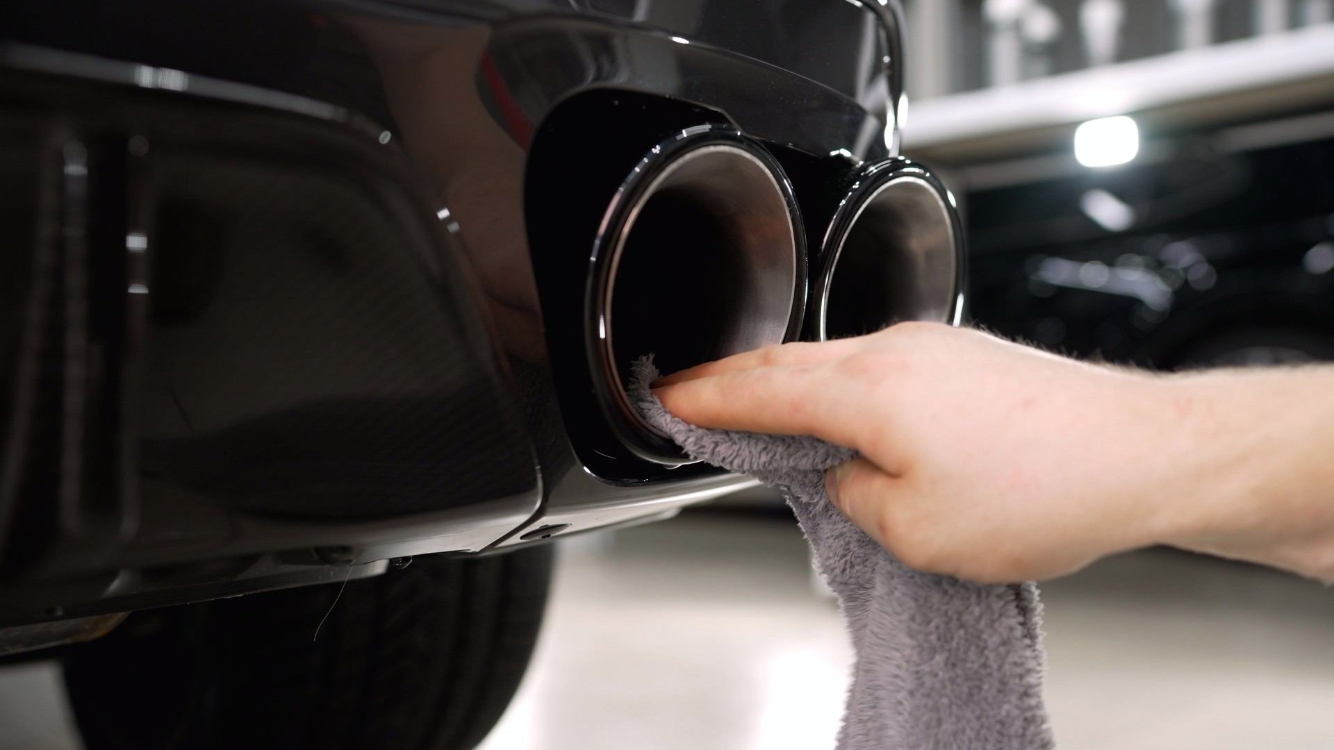 Man is wiping, cleaning and polishing by cloth chrome exhaust pipes of modern automobile, close-up. The master wipes the exhaust pipe with a rag.